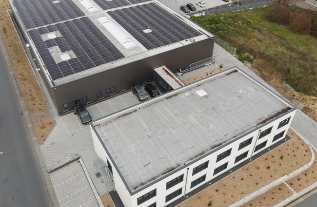 Luftaufnahme einer Gewerbehalle mit Photovoltaikanlage auf dem Flachdach und angeschlossenem Bürogebäude