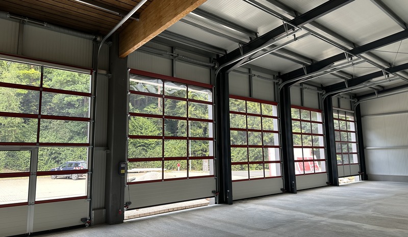 Innenansicht einer Stahlhalle mit vier verglasten Sektionaltoren und Holzbinder